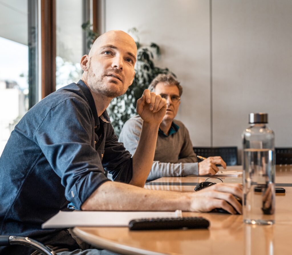 Mitarbeitende der Gossweiler Ingenieure AG an einem Sitzungszimmertisch mit Fokus auf den Monitor