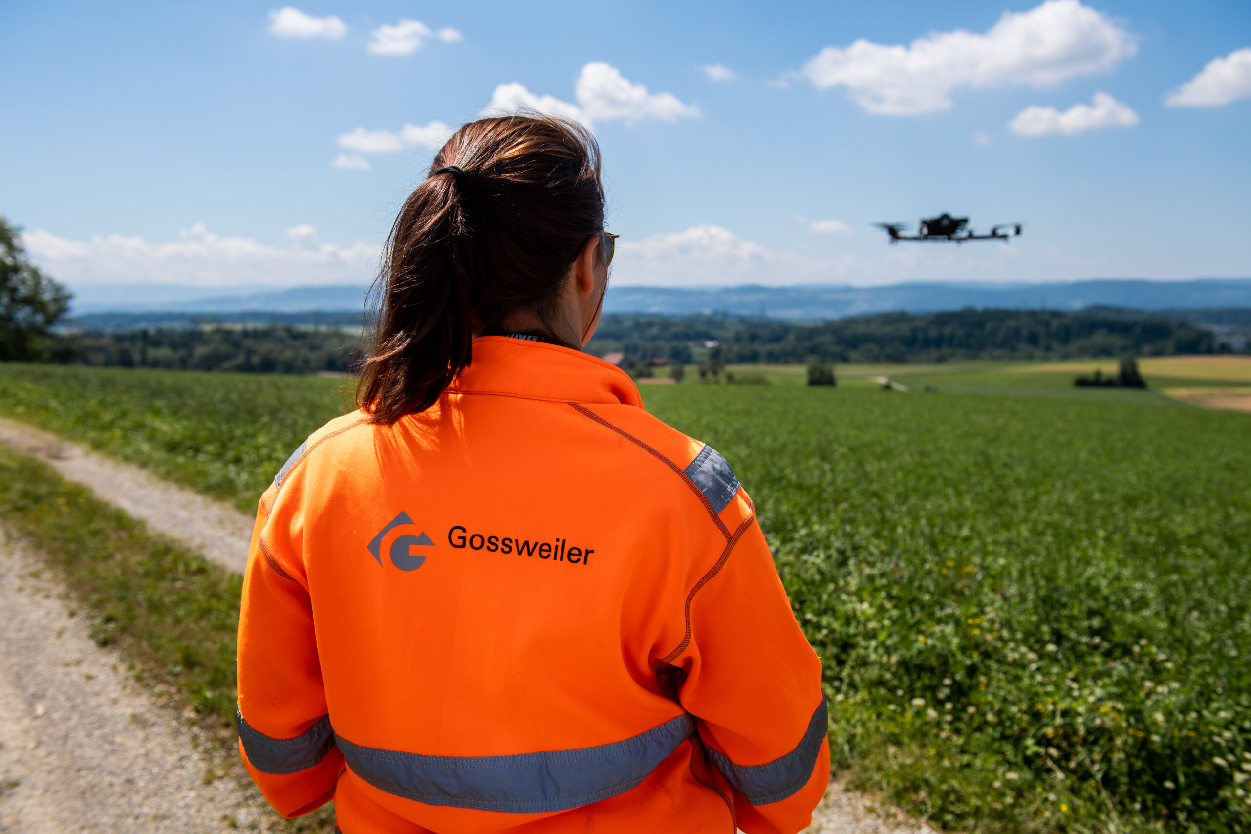 Mitarbeiterin der Gossweiler Ingenieure in oranger Kleidung bedient eine Drohne.