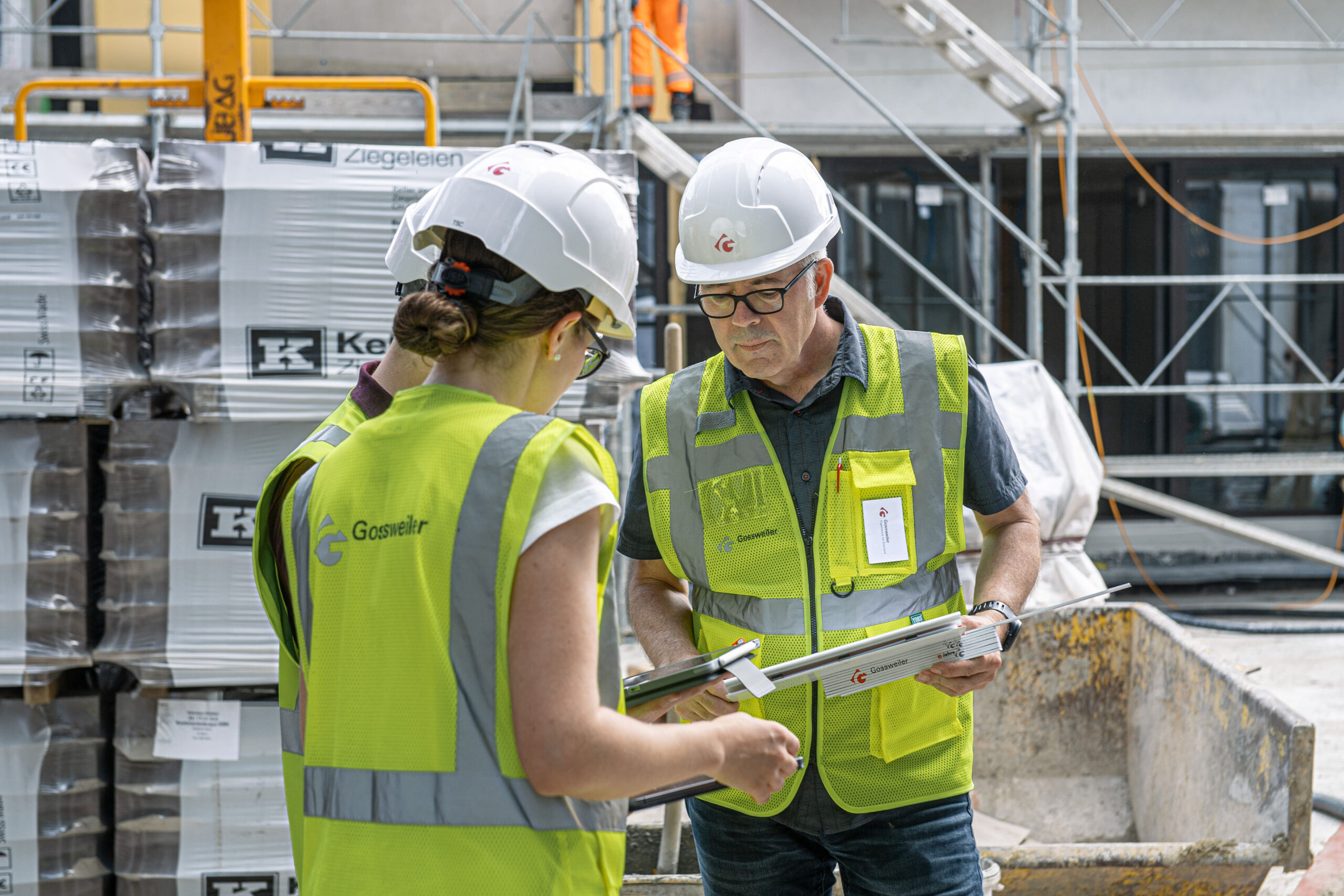 Mitarbeitende der Gossweiler Ingenieure mit Bauhelm und gelber Weste vor einer Baustelle.